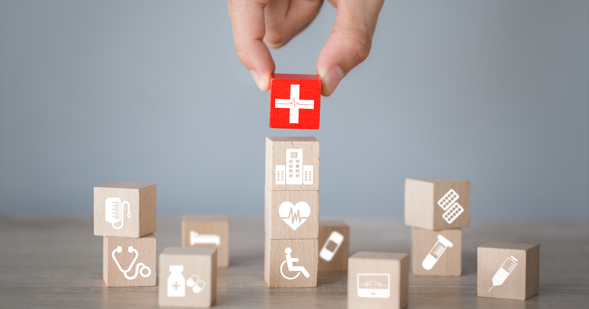 Hand stacking blocks with symbols where the last one placed is all red with a hospital symbol